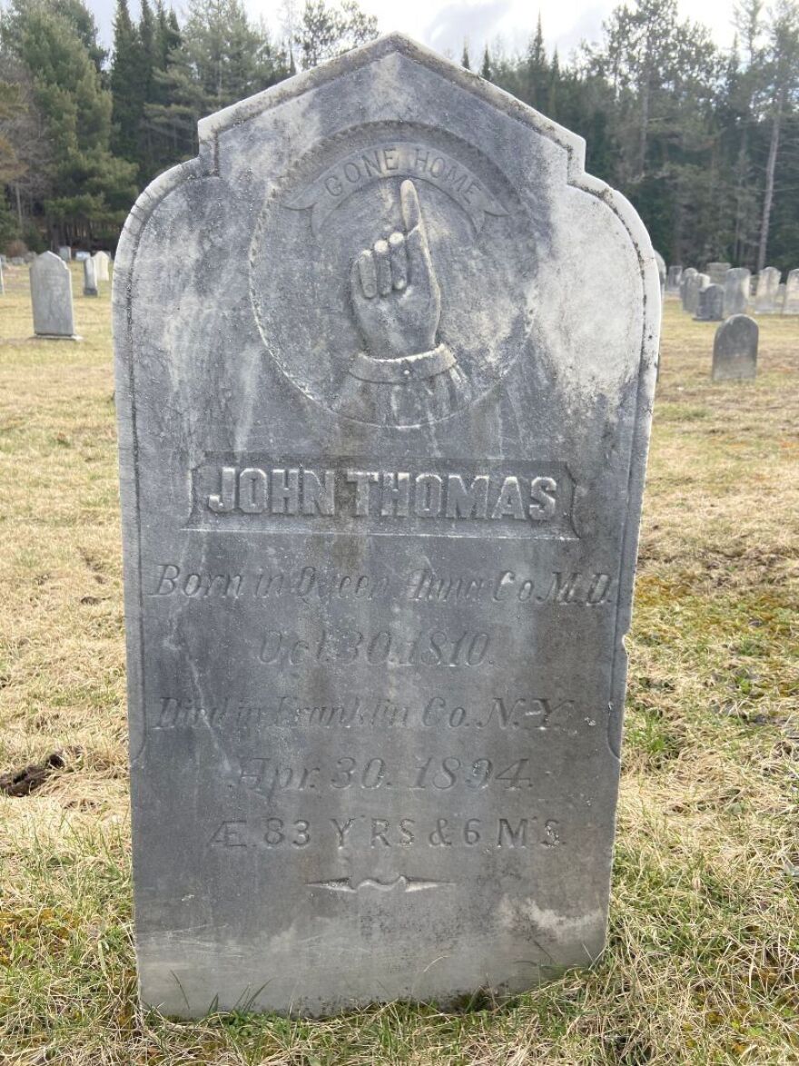 A gray, rounded tombstone for John Thomas.