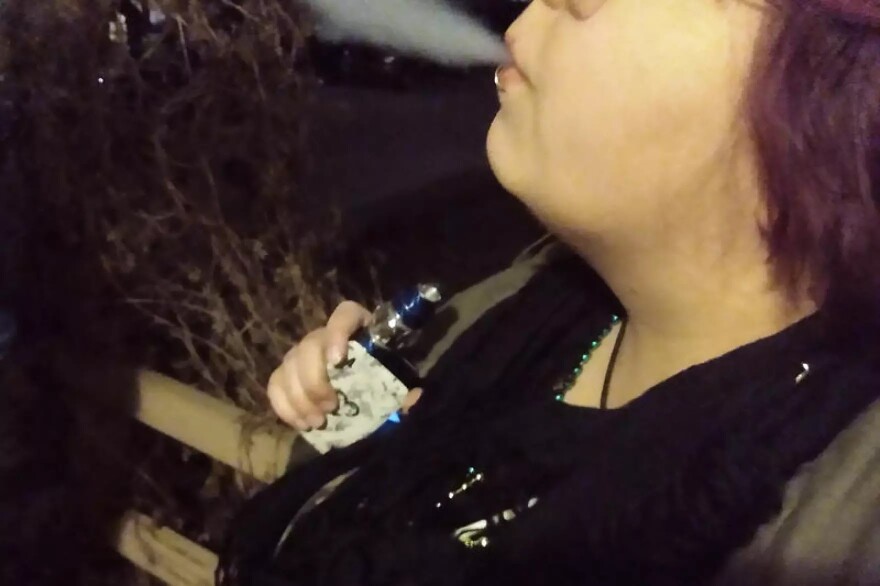 A person sits vaping on a porch 