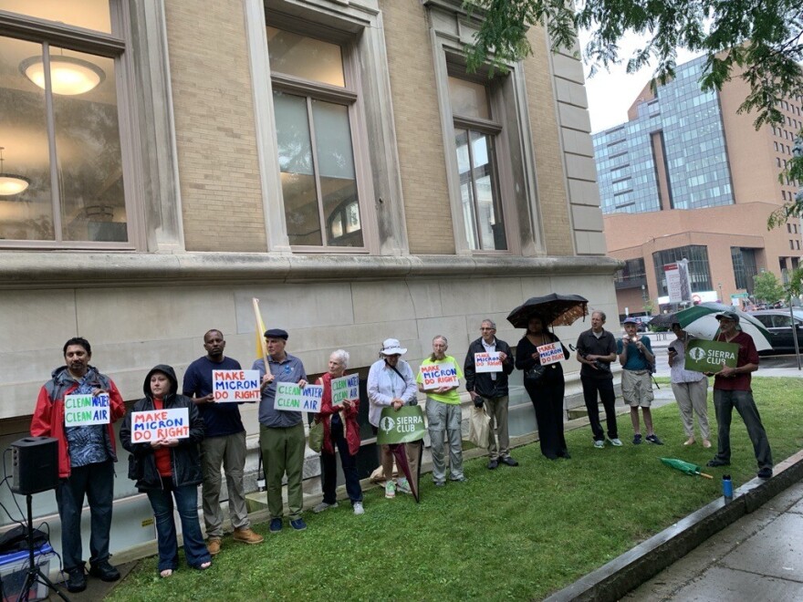 Thirteen people stand in a line in the rain holding signs outside of the Onondaga County Industrial Development Agency’s Office demanding Micron’s 45-day public comment period be extended.