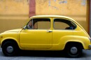 A vintage yellow car is parked in front of a cracking mustard and red painted wall.
