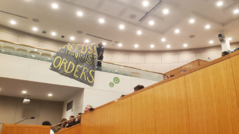 At a CMS school board meeting, an attendee unfurls a banner to protest ICE at schools.