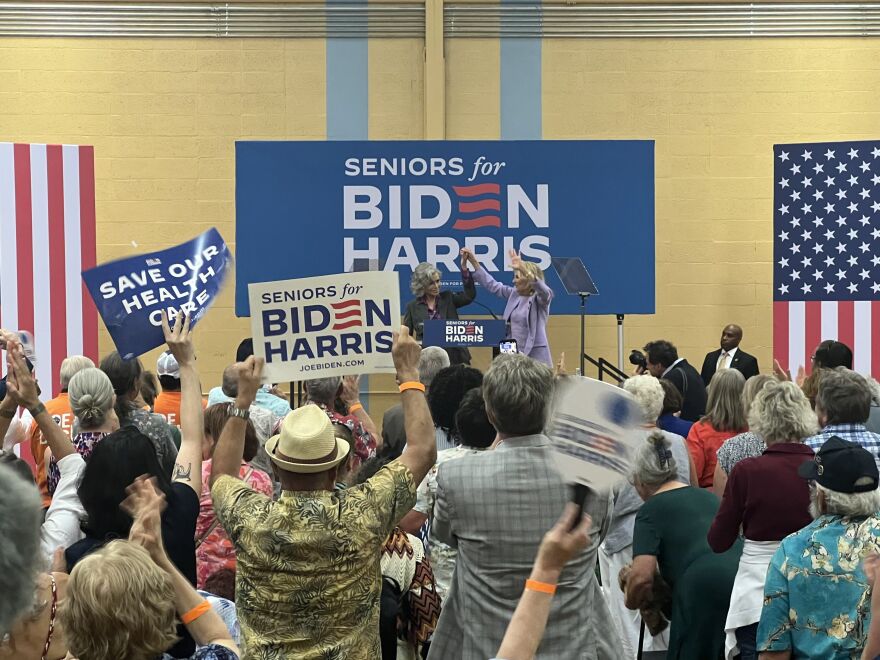 Biden and Fonda raise and embrace hands while on a stage as a crowd of people cheer them on.