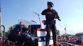 A man in a suit standing on a podium, armed with a gun