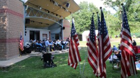 American flags line the grass beside the amphitheater stage, where band members perform under the pavilion roof.
