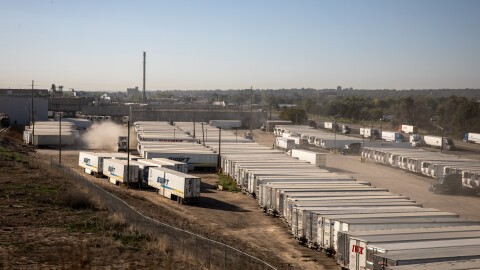 This photo taken outside the JBS meatpacking plant in Greeley, shows dozens of large semi trucks in a dirt parking lot. Some of the trucks read "Swift" on the side.