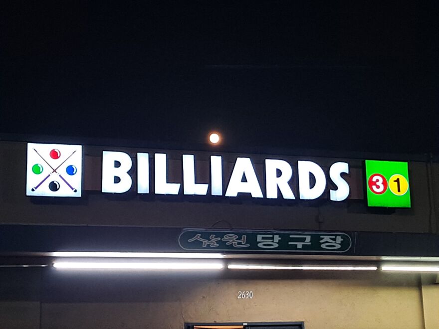 A neon sign at night that says 'Billiards 31' with a full moon above it 
