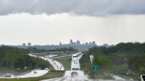 A dark cloud looms over a city skyline while cars on highways in foreground drive on slickened roads