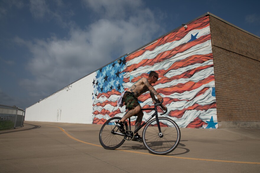 A man bikes past an American flag mural, in the Design district in Dallas. 