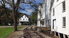 A railroad track curves by several white, wooden buildings.