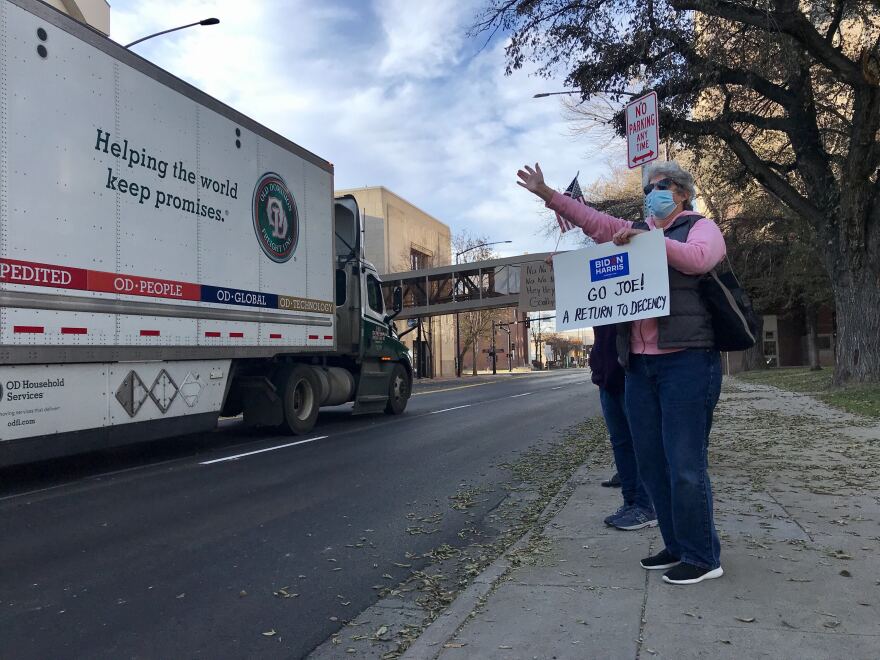 A woman stands on the side of 27th St. in downtown Billings holding a homemade sign that reads "Go Joe! A return to decency."