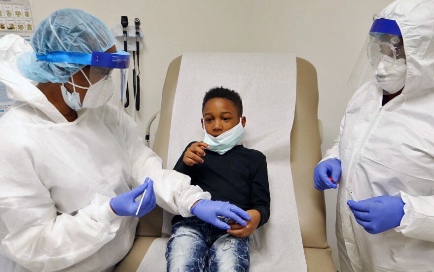 Nurse Nellie Smith, left, holds down the hand of 8-year-old Kayden Tree, before inserting a swab into his nose during a coronavirus test at a CareSTL Health testing site in St. Louis in May.