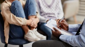 A psychologist takes notes on a clipboard in a therapy session for children.