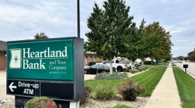 A Heartland Bank and Trust sign directs customers toward the ATM in front of a row of trees.