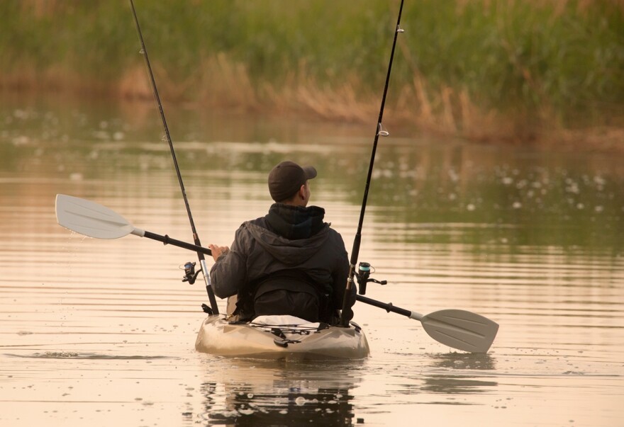 A man use an oar in his kayak with two fishing rods sticking up