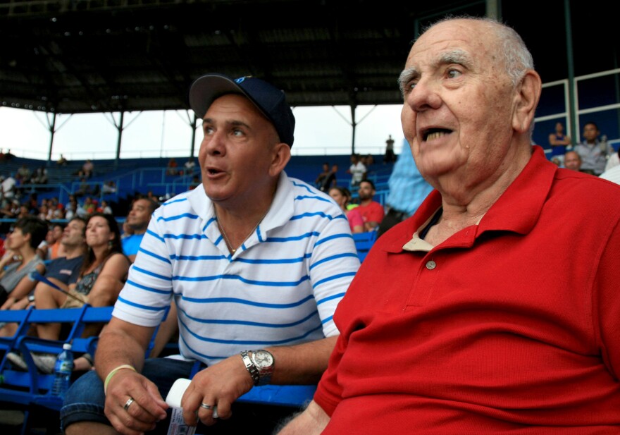 Ismael Sené (right), a former intelligence agent-turned-baseball historian, watches a game at Latin American Stadium.