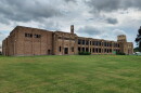 An elongated old brick school building on a slight grassy hill on an overcast day.
