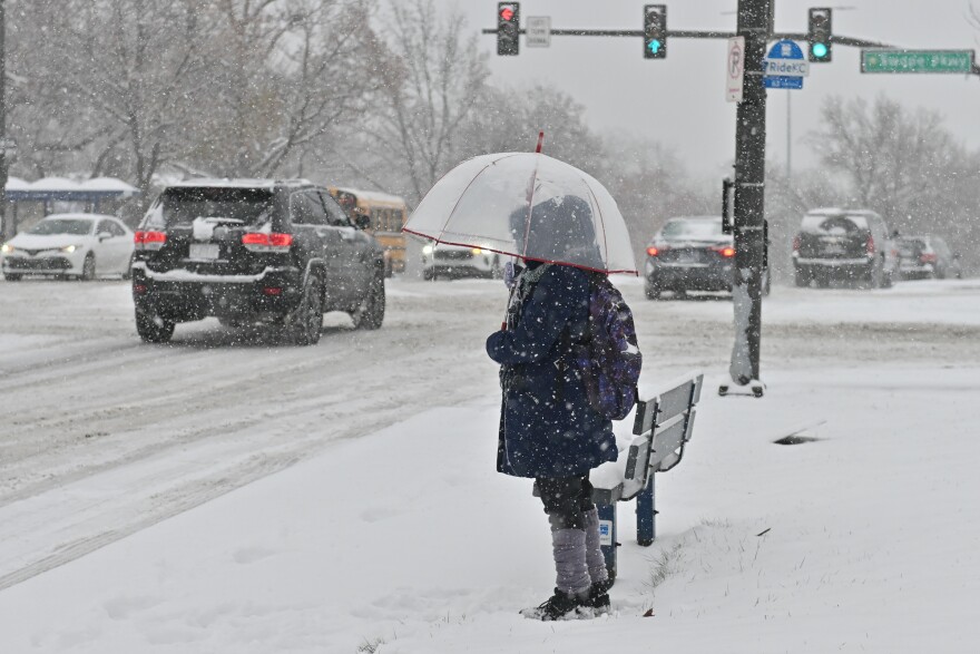 On Dec. 1, 2025, Dimple Dennis uses an umbrella to fend off falling snow while waiting at a bus stop at 63rd and Swope Parkway to go to the grocery store.