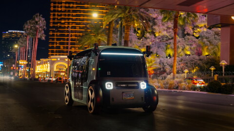 A black and green robotaxi going down the road with casinos in the background