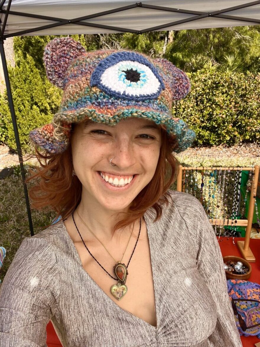 Woman wearing a colorful hat and smiling with plants in the background