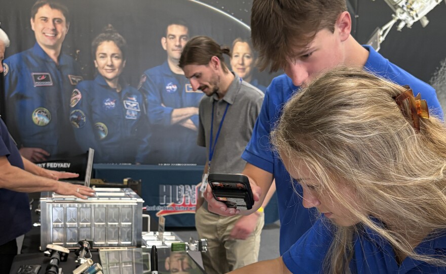 Two young people stand in front of a poster showing several astronauts.