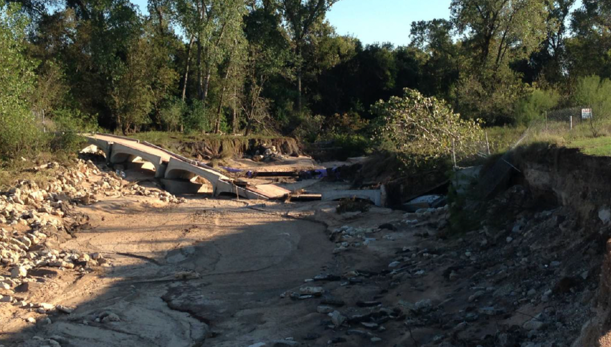 A bridge collapsed into a dry creek bed. The bottom of the creek is lined with sand.