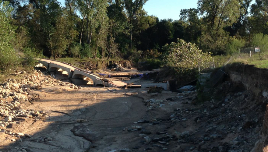 A bridge collapsed into a dry creek bed. The bottom of the creek is lined with sand. 