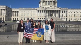 Seven people stand in front of the U.S. Capitol. They are holding a joint U.S./Ukrainian flag.