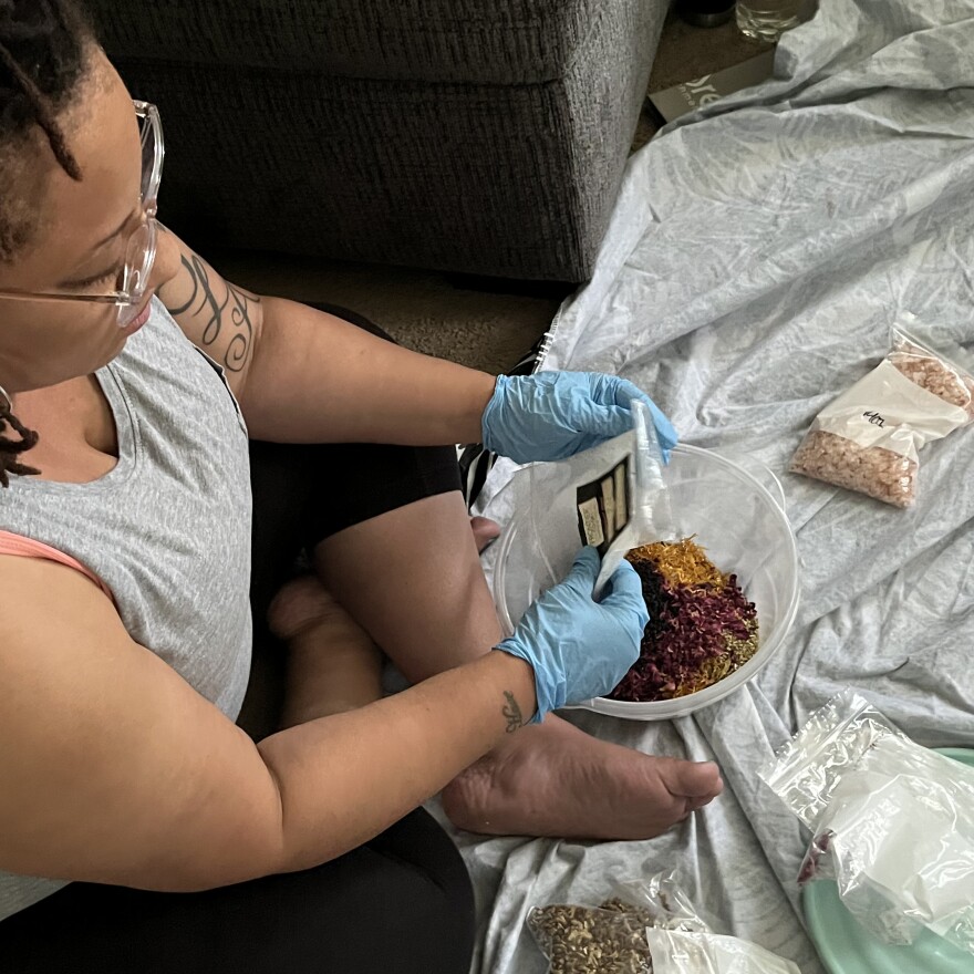 Erica Dickson sits cross-legged on the floor of a home while she prepares a bowl of herbs for use in her doula practice.