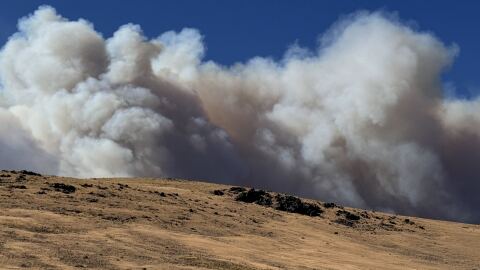 A hilly terrain with smoke filling an otherwise blue sky.