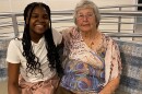 A Black teenage girl with long hair and a gray haired white woman sit together and smile