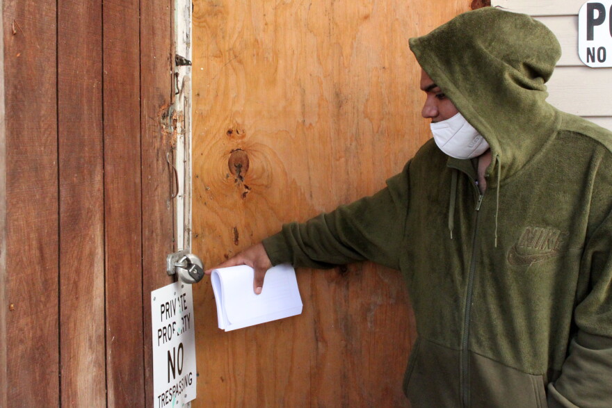 A New York tenant standing at a locked property entrance while holding legal papers.