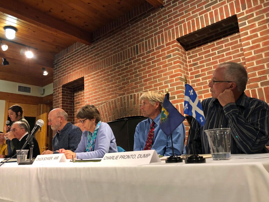 Monday evening, a citizen group called Don't Undermine Memphremagog's Purity (DUMP) held a panel discussion about a proposed expansion of the Coventry landfill. The panelists sit along a table in front of a brick wall while one speaks.