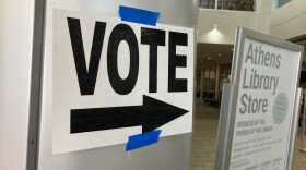a white sign with "VOTE" and an arrow, printed boldly in black, pasted to a door, directing voter traffic at a library.