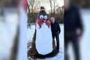 A man stands next to a tree that is disguised as a penguin on a snowy February day.
