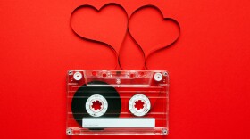 Vintage audio cassette with loose tape shaping two hearts on red background