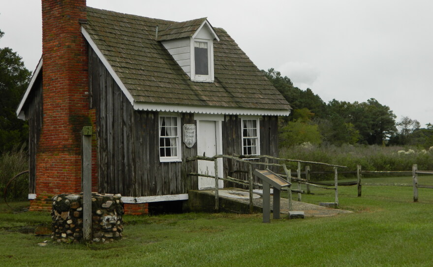 A small, worn, single room cottage. A brick chimney on the left outer wall and a stone well. 