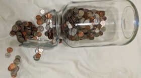 A glass coin jar, with coins spilling out from the left.
