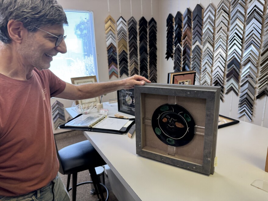 Man holds a Picasso plate artwork held by pegs in square frame