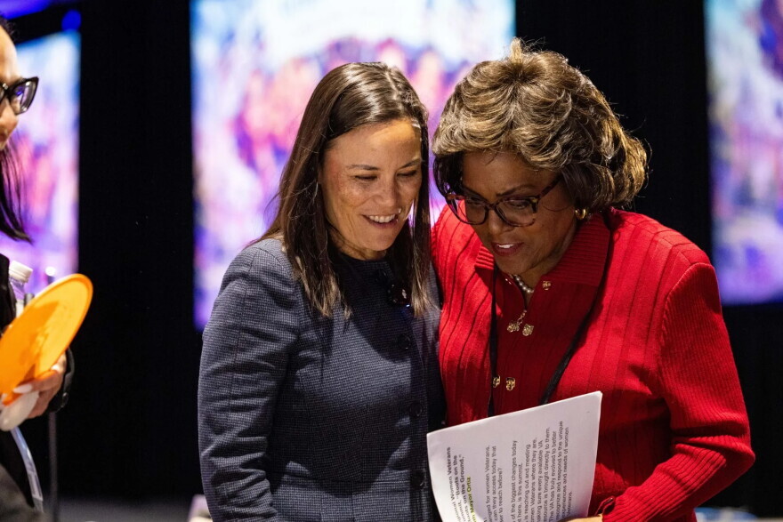 Two women confer inside a conference center.
