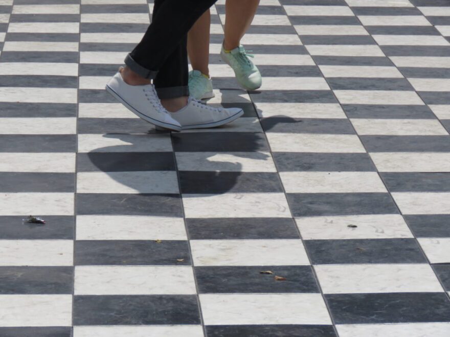 Two dancers feet move across a checkered dance floor.