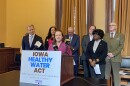 Seven people stand by a podium with a sign that reads 'Iowa Healthy Water Act'