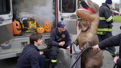 Staff from Kenai Fire Department fill a dinosaur's bag with candy at the Trunk-or-Treat hosted by the Boys and Girls Clubs of the Kenai Peninsula on Saturday, Oct. 24, 2026, in Kenai, Alaska.