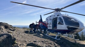 Search and Rescue personnel help load an injured hiker into a Life Flight helicopter that is perched atop a butte.