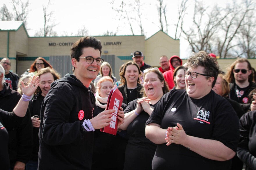 People wearing black t-shirts and hoodies smile while one person holds a red envelope