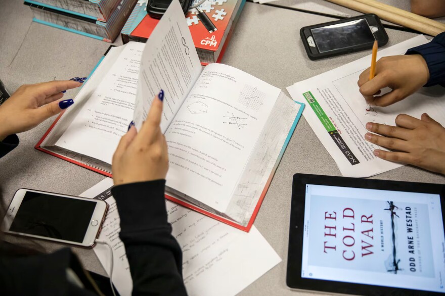 Open book and school materials are scattered across a school classroom table.