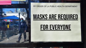 A man wearing a protective face mask walks past a sign requiring face masks posted on a storefront in Los Angeles, California.