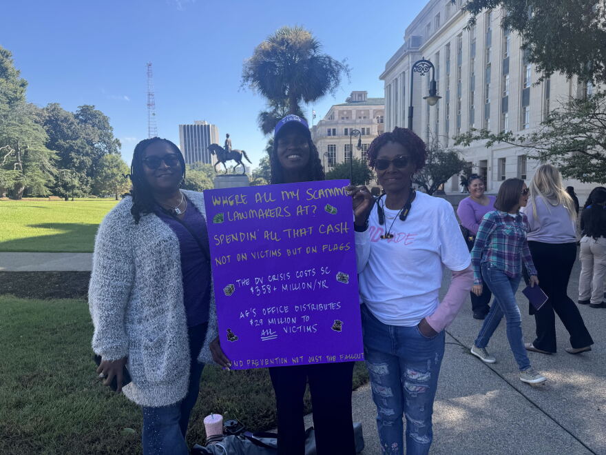 Domestic violence survivor Jamie Banks holds a sign with friends during the 2026 Silent Witness Ceremony on the Statehouse grounds in Columbia on Oct. 6, 2026.