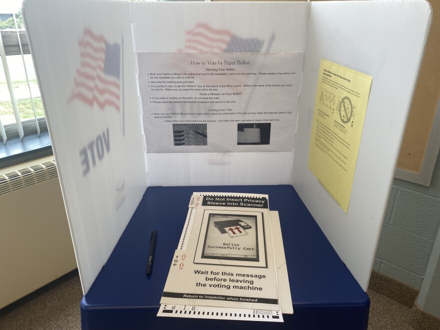 A blue table with a ballot surrounded by a white privacy screen.  