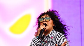 Remi Wolf sings onstage with a purple background behind her. 
