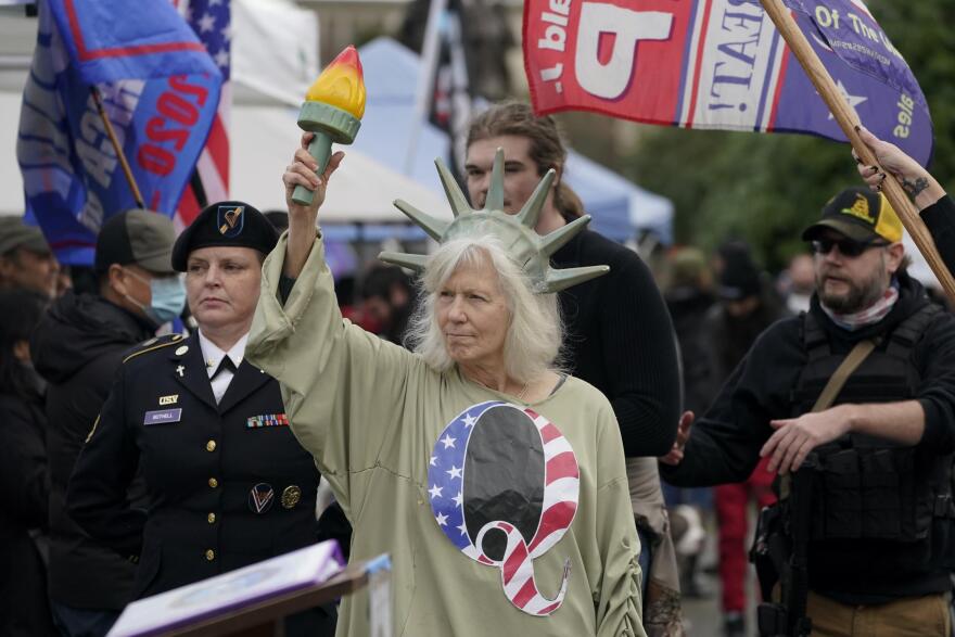 A person dressed as Lady Liberty wears a shirt with the letter Q, referring to QAnon, as protesters take part in a protest, Wednesday, Jan. 6, 2021, at the Capitol in Olympia, Wash.